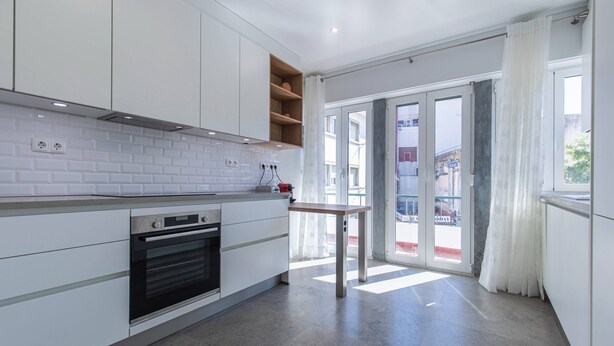 Eine moderne Küche mit weißen Schränken, einem eingebauten Backofen und einem kleinen Tisch.