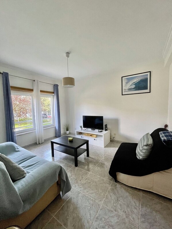 A living room with a sofa, a coffee table, a TV on a stand, and a painting on the wall.