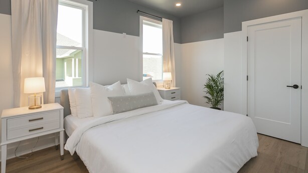 A bedroom with a large bed, two bedside tables with lamps, a potted plant, and a door.