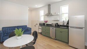 A modern kitchen with green cabinets, a white refrigerator, and a blue sofa.