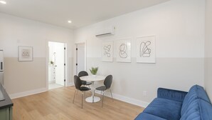 A modern living room with a blue sofa, a round dining table with four chairs, and abstract wall art.
