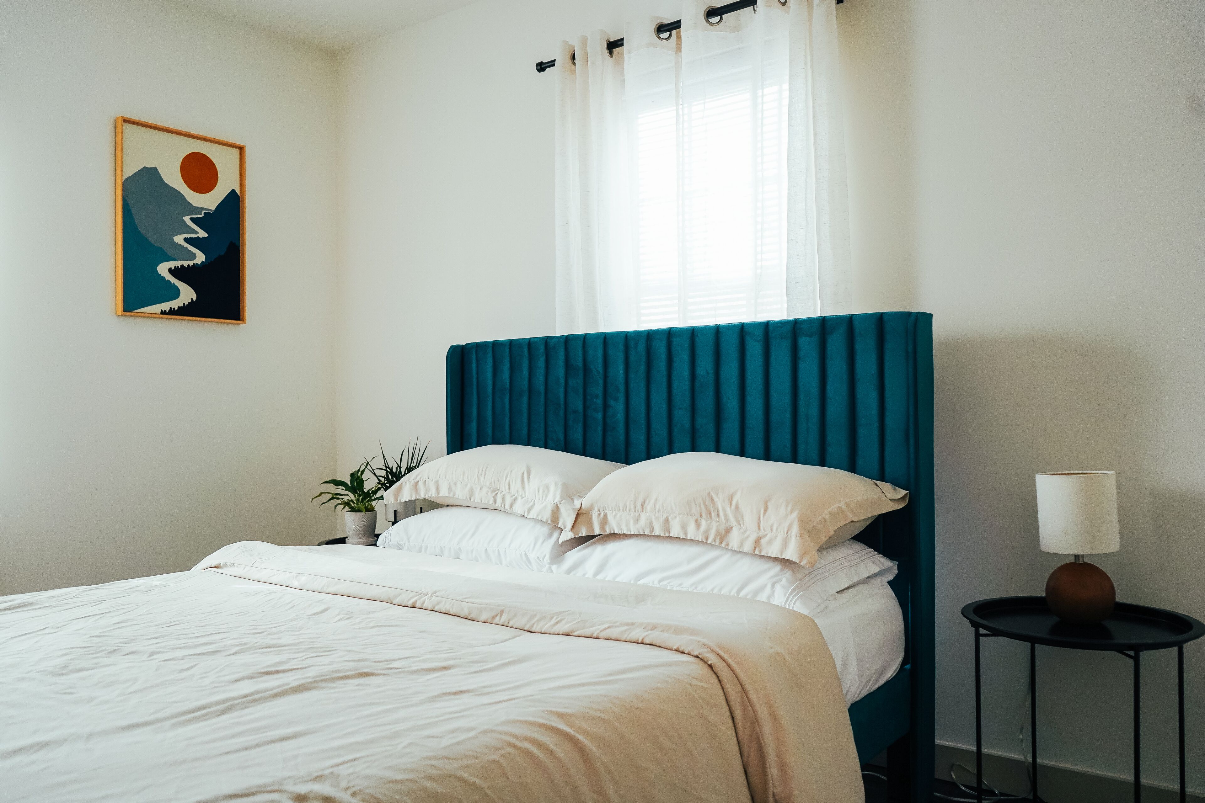 A neatly made bed with white bedding, a teal headboard, and a single bedside table with a lamp.
