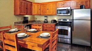 Una cocina con armarios de madera, un refrigerador de acero inoxidable, un microondas, una estufa y una mesa de comedor con platos y vasos.