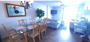 Uma sala de jantar com mesa de vidro e cadeiras de madeira, um sofá e uma televisão na parede.