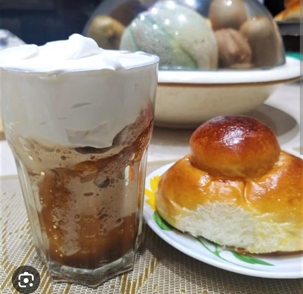 A glass of iced coffee with whipped cream and a plate with a glazed bun.