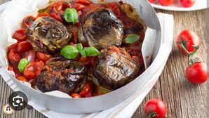 Un plat d’aubergines farcies, servi dans un bol blanc, accompagné de tomates cerises et de basilic.