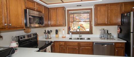 A kitchen with wooden cabinets, stainless steel appliances, a dishwasher, and a window with a view.