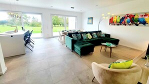 A spacious living area with a green sofa, a dining table, and a kitchen area with a sink and chairs. - Spacious & Luxurious 5 bedrooms House (Reckange-sur-Mess)