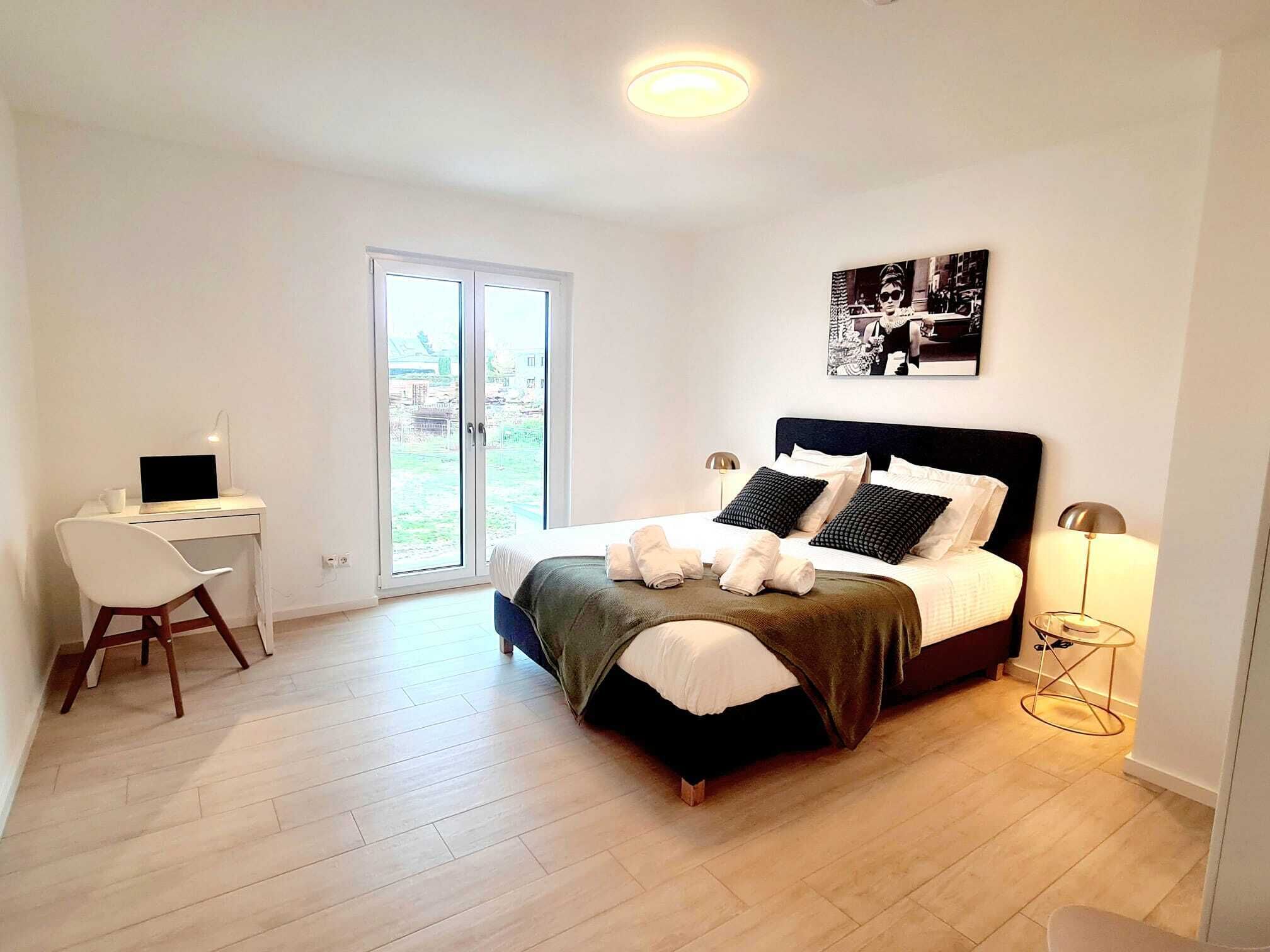 Une chambre à coucher avec un lit, un bureau, une chaise, une lampe et un tableau au mur.