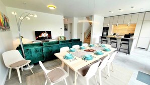 A modern living space with a dining area, a green sofa, a TV, and a kitchen. - Spacious & Luxurious 5 bedrooms House (Reckange-sur-Mess)