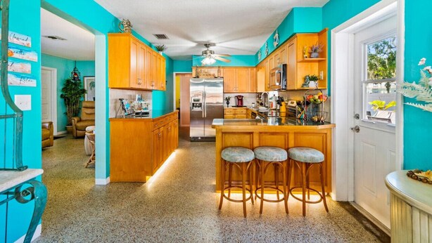 Eine Küche mit Holzausstattung, einem Edelstahlkühlschrank, einer Bar mit Hockern und einer türkisblauen Wand.