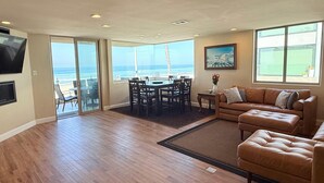 A spacious living room with a large window overlooking the ocean, a dining area with a table and chairs, and a leather sofa. - Surf View-2 Decks with Ocean views, Garage (San Diego)