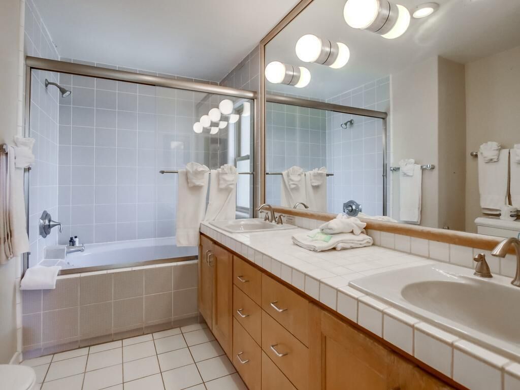 A modern bathroom with a bathtub, two sinks, a large mirror, and a shower area.