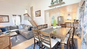 Un salón espacioso con comedor, una escalera y una cocina visible a través de un umbral abierto.