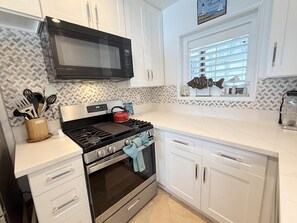 Een keuken met witte kastjes, een magnetron, een fornuis en een raam met decoratieve vissen.