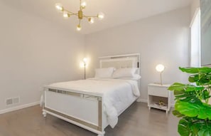 A bedroom with a white bed, bedside tables with lamps, and a large green plant. - Beautiful 3bedroom apartment (Elizabeth)