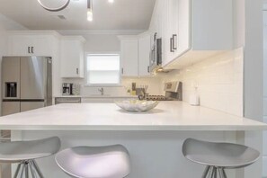 A modern kitchen with white cabinetry, a large island with bar stools, stainless steel appliances, and a window providing natural light. - Beautiful 3bedroom apartment (Elizabeth)
