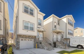 A two-story residential building with a stone facade, a garage, and a front entrance with a staircase. - Beautiful 3bedroom apartment (Elizabeth)