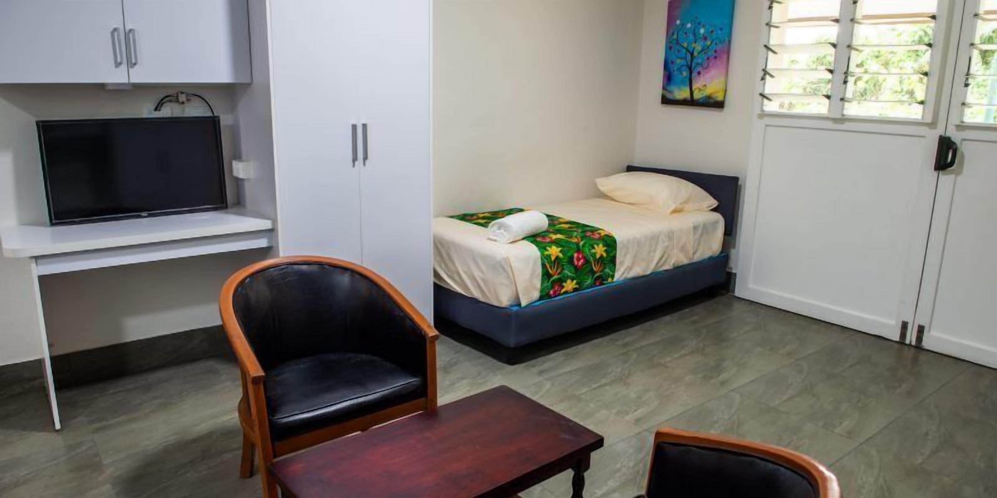 A bedroom with a bed, a chair, a table, a TV, and a painting on the wall.