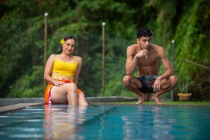 A poolside scene with two individuals, one seated and one squatting, surrounded by lush greenery. - Yatu Lau Hotel & Conference (Suva)