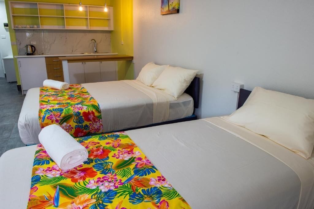 A hotel room with two beds, a small kitchenette, and a bathroom.