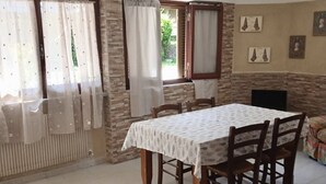 Un comedor con una mesa y sillas, una ventana con cortinas, una chimenea y cuadros colgados en la pared.