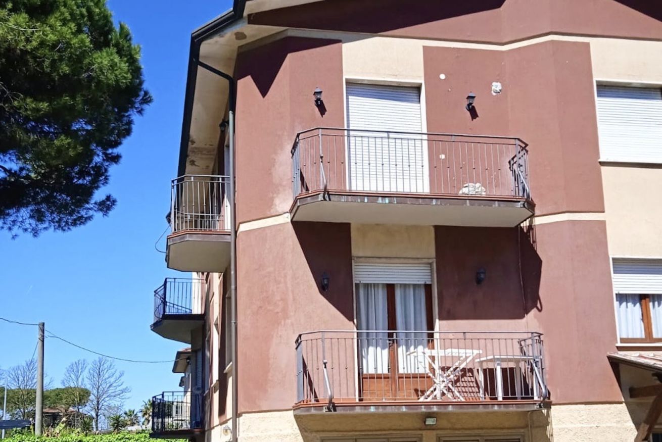 A multi-story residential building with balconies, a garage door, and a clear sky.