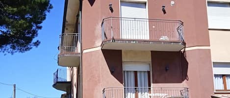 Un edificio residencial de varios pisos con balcones, una puerta de garaje y cielo despejado.