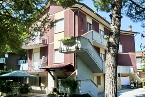 Un edificio de varios pisos con balcones, mobiliario exterior y un árbol en primer plano.