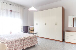 Een slaapkamer met een bed, een kledingkast, een stoel en een nachtkastje.