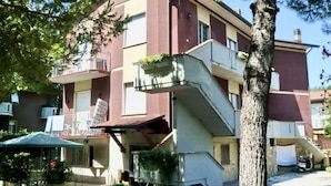Ein mehrstöckiges Gebäude mit Balkonen, einer Treppe und Außenbestuhlung.