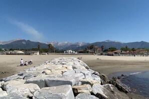 A beach with large rocks in the foreground, a sandy beach, and mountains in the background.