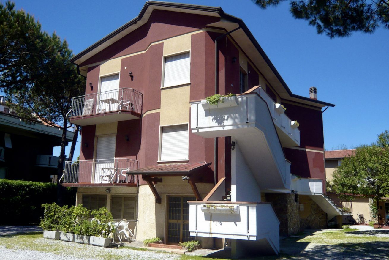 A multi-story building with a balcony on the second floor, a small front porch, and a garage.