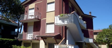 Un edificio de varios pisos con un balcón en el segundo piso, un pequeño porche delantero y un garaje.