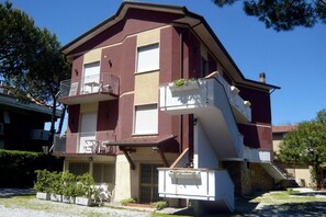 A multi-story building with a balcony on the second floor, a small front porch, and a garage.