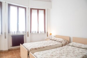 Een kamer met twee bedden, een radiator en een raam met gordijnen.