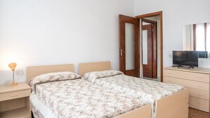 Quarto com cama, penteadeira, televisão e porta que dá para outro cômodo.