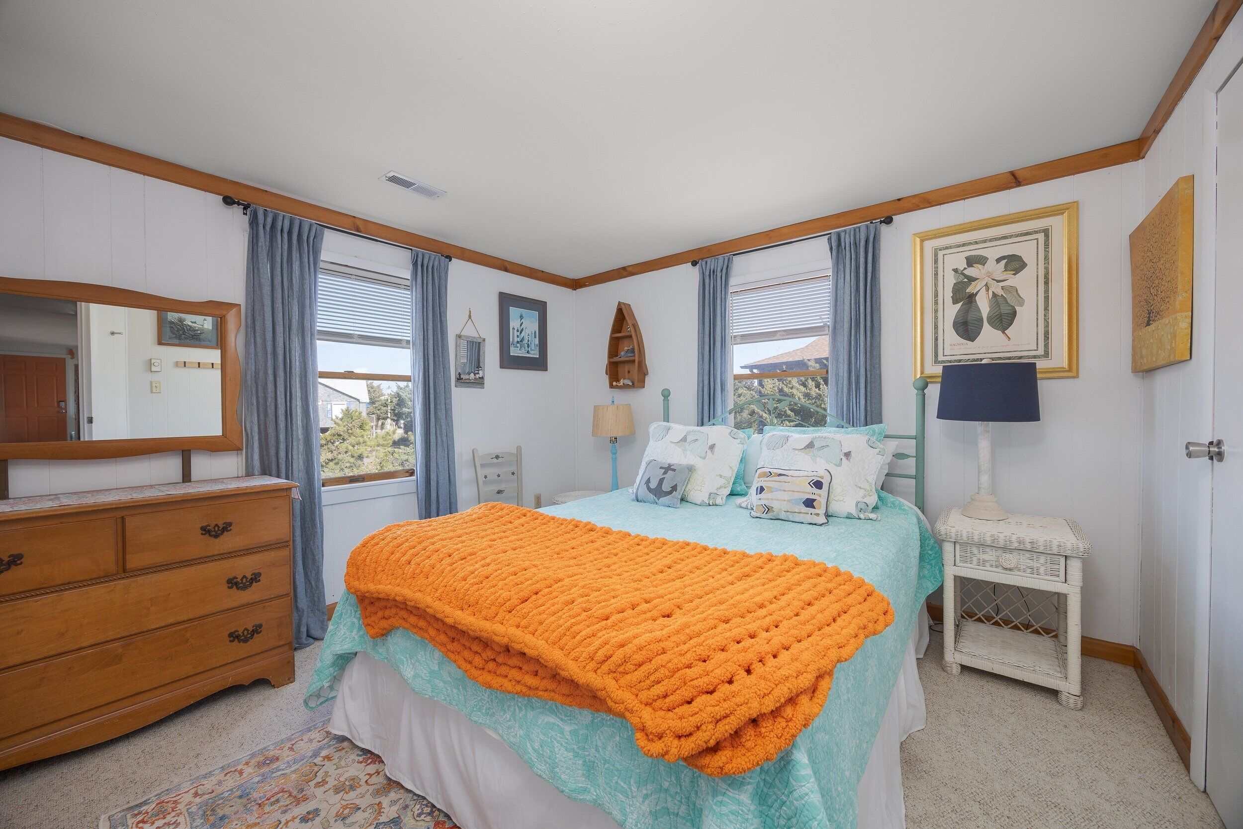 A bedroom with a bed, dresser, nightstand, and a window with curtains.