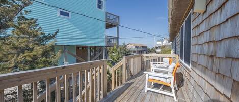 A wooden deck with a white chair and a small table, overlooking a blue building with a balcony.