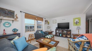 Ein Wohnzimmer mit einer Couch, Sesseln, einem Couchtisch, einem Fernseher und einem Bücherregal.