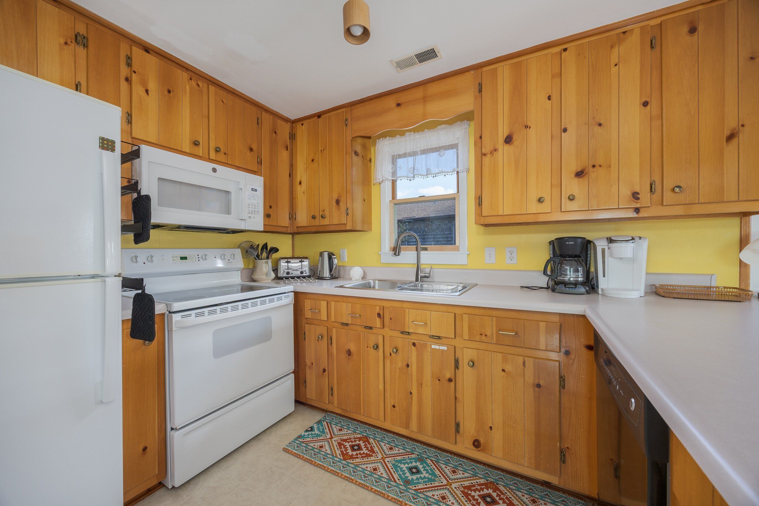 A kitchen with wooden cabinets, a white refrigerator, a microwave, a stove, a sink, and a coffee maker.