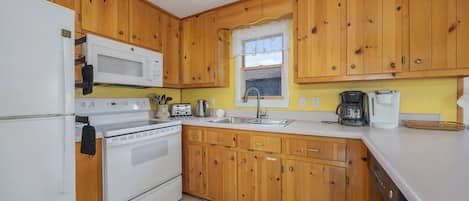 Une cuisine avec des meubles en bois, un réfrigérateur blanc, un four à micro-ondes, une cuisinière, un évier et une machine à café.
