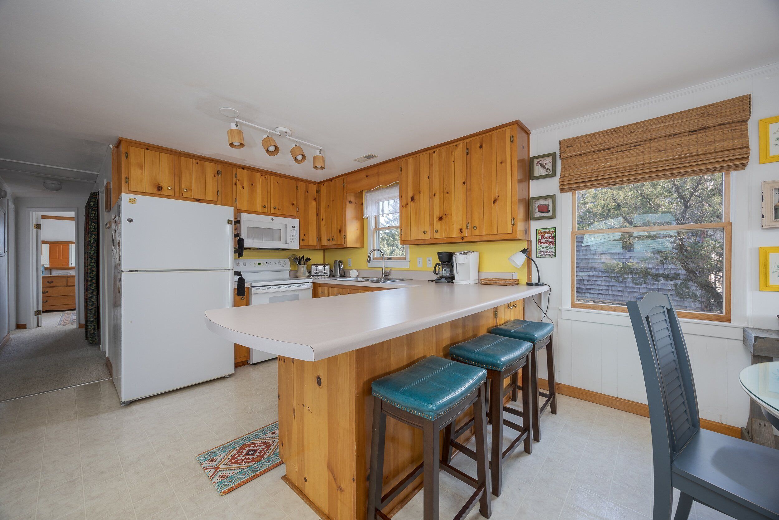 A kitchen with wooden cabinets, a white refrigerator, a microwave, and a bar area with stools.