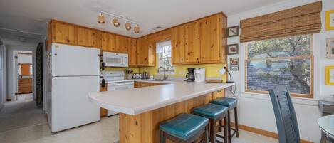 A kitchen with wooden cabinets, a white refrigerator, a microwave, and a bar area with stools.