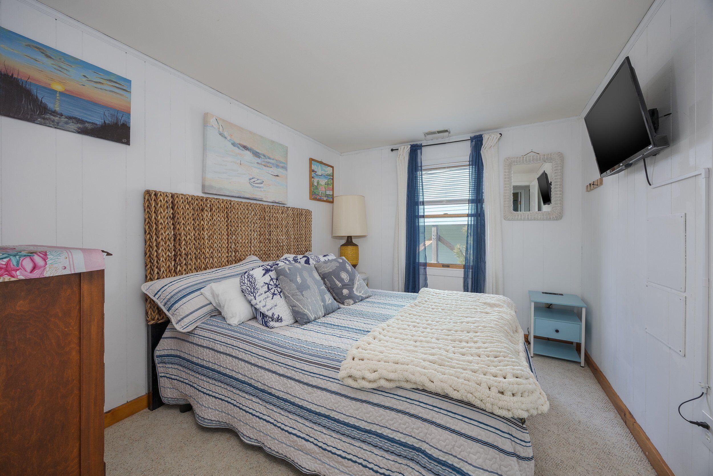 A bedroom with a bed, a bedside table, a lamp, a TV, and artwork on the walls.