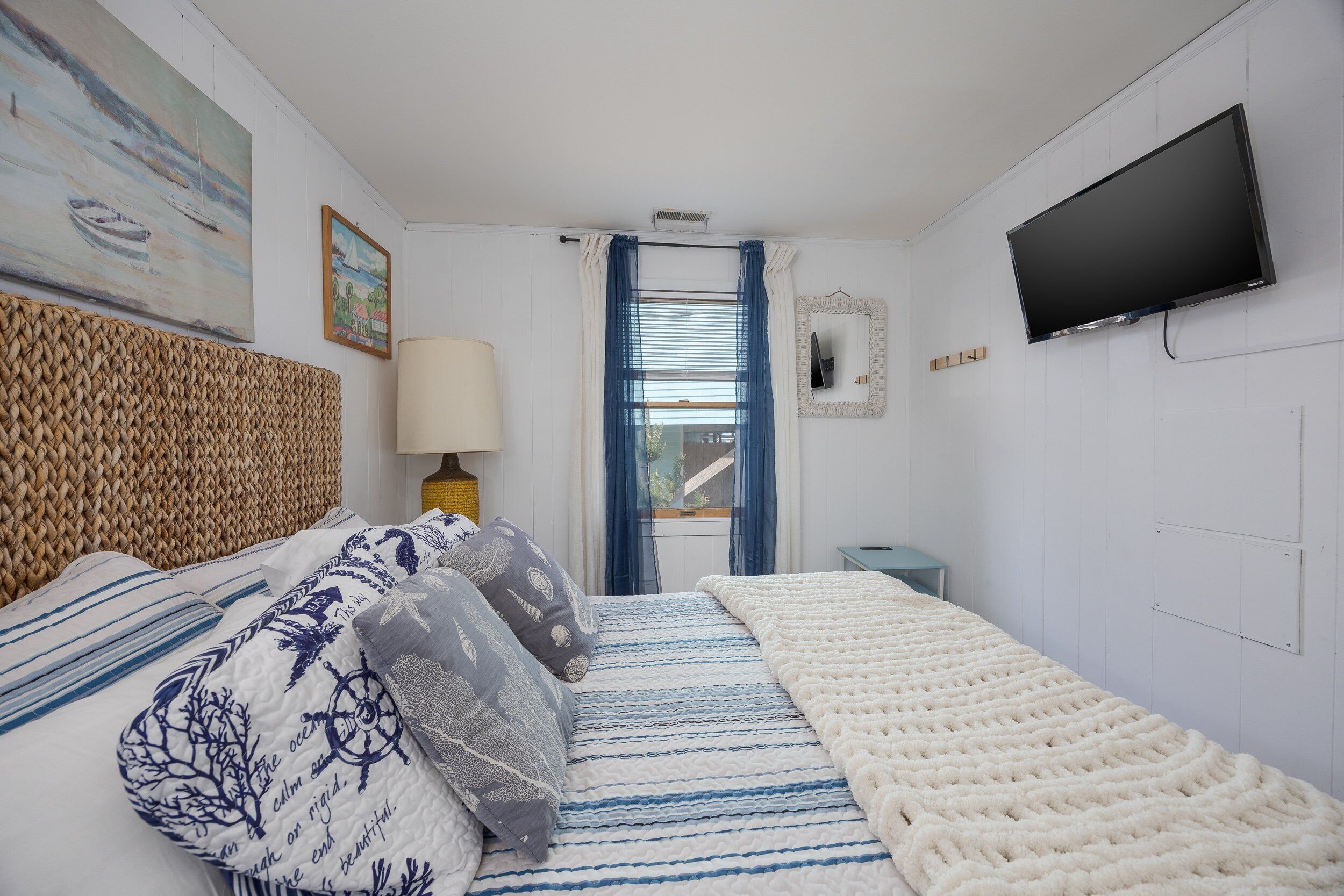 A bedroom with a bed, a TV, a window with curtains, and a painting on the wall.
