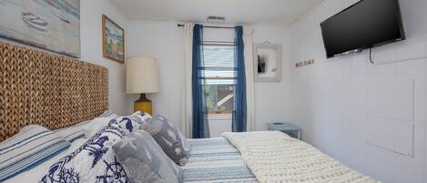 Quarto com uma cama, TV, janela com cortinas e um quadro na parede.
