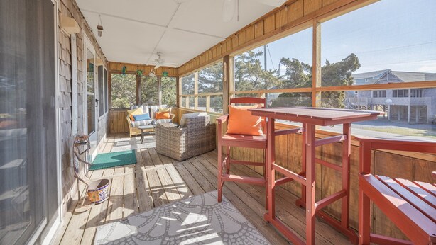 Eine überdachte Veranda mit Tisch und Stühlen, ein Rattansofa und Blick ins Freie.
