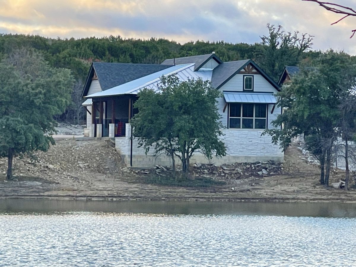 Uma casa com telhado inclinado, varanda frontal e vista para um lago.