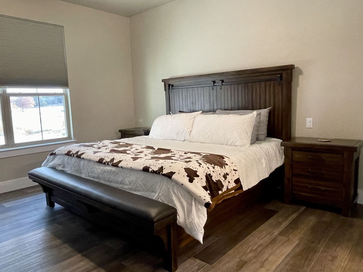 Quarto com cama, banqueta, mesas de cabeceira e uma janela.